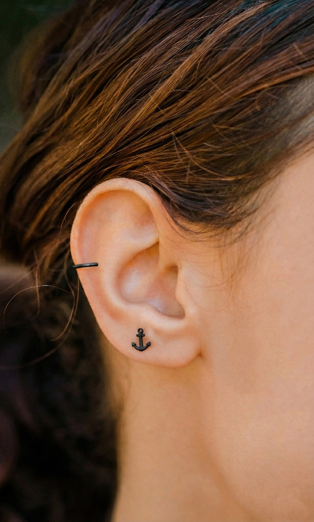 Close-up of an ear with a black anchor-shaped earring.