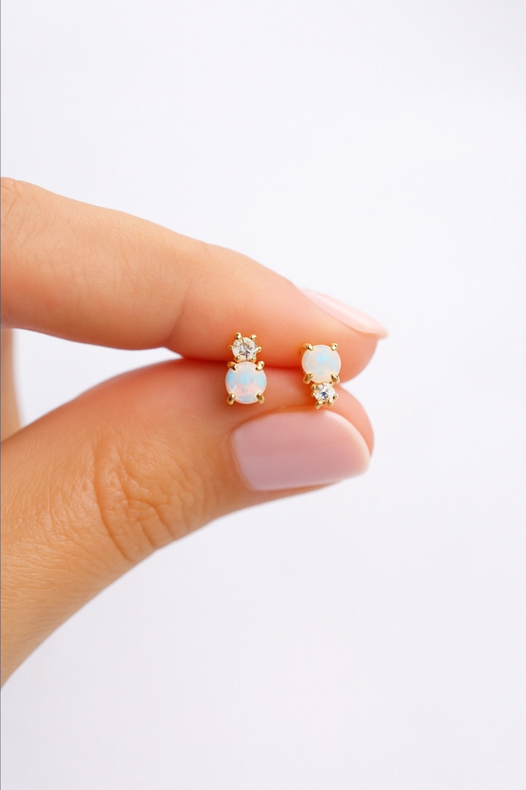 Opal stud earrings held between fingers against a white background