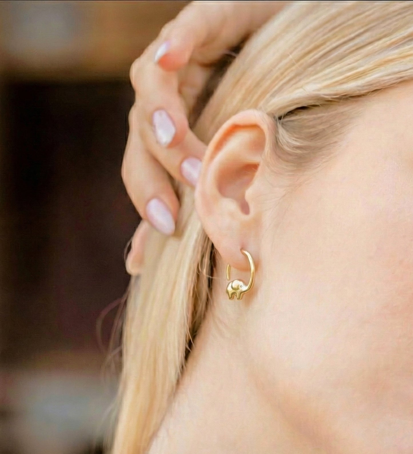 Close-up of a person wearing a gold elephant earring with a blurred background