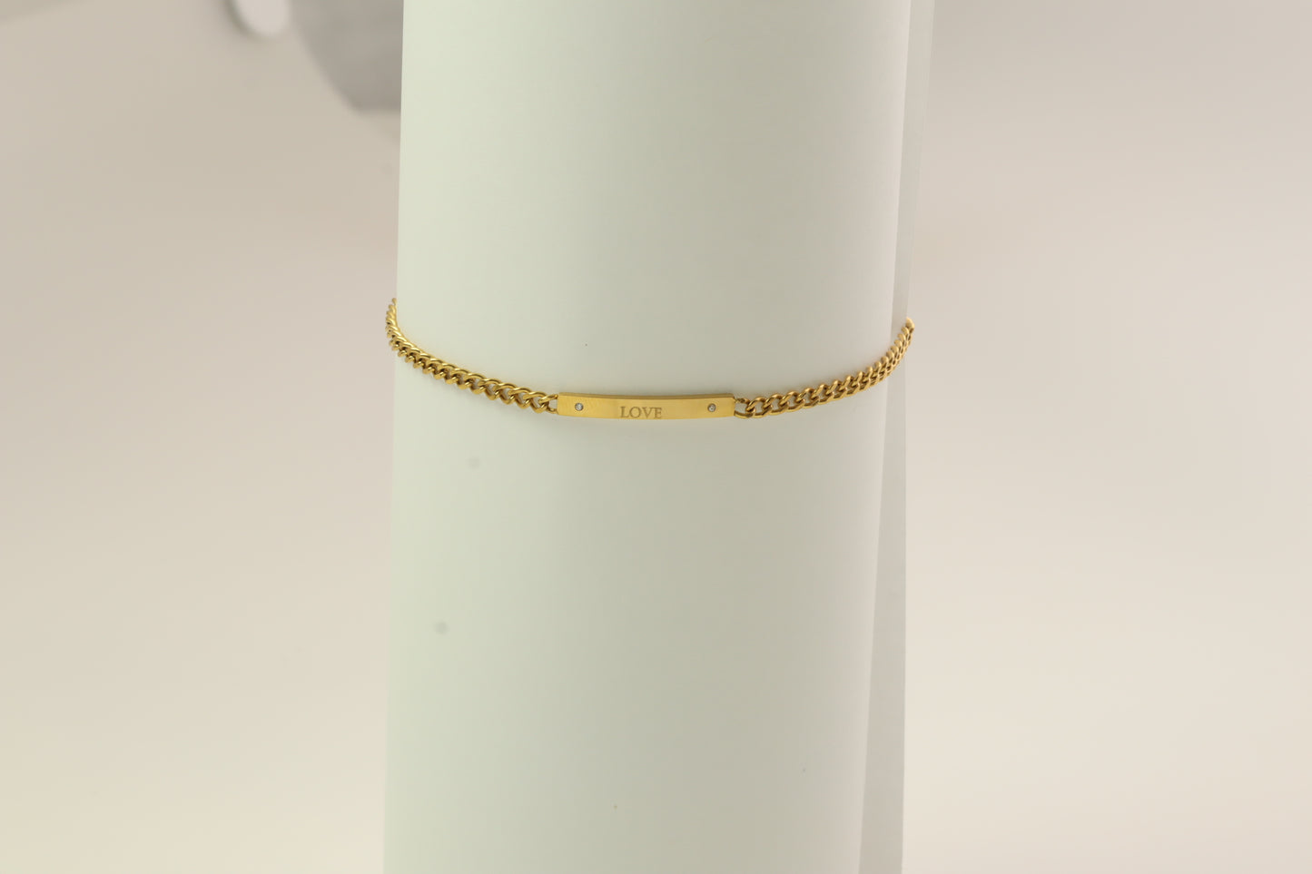 Gold bracelet on a mannequin arm against a light background