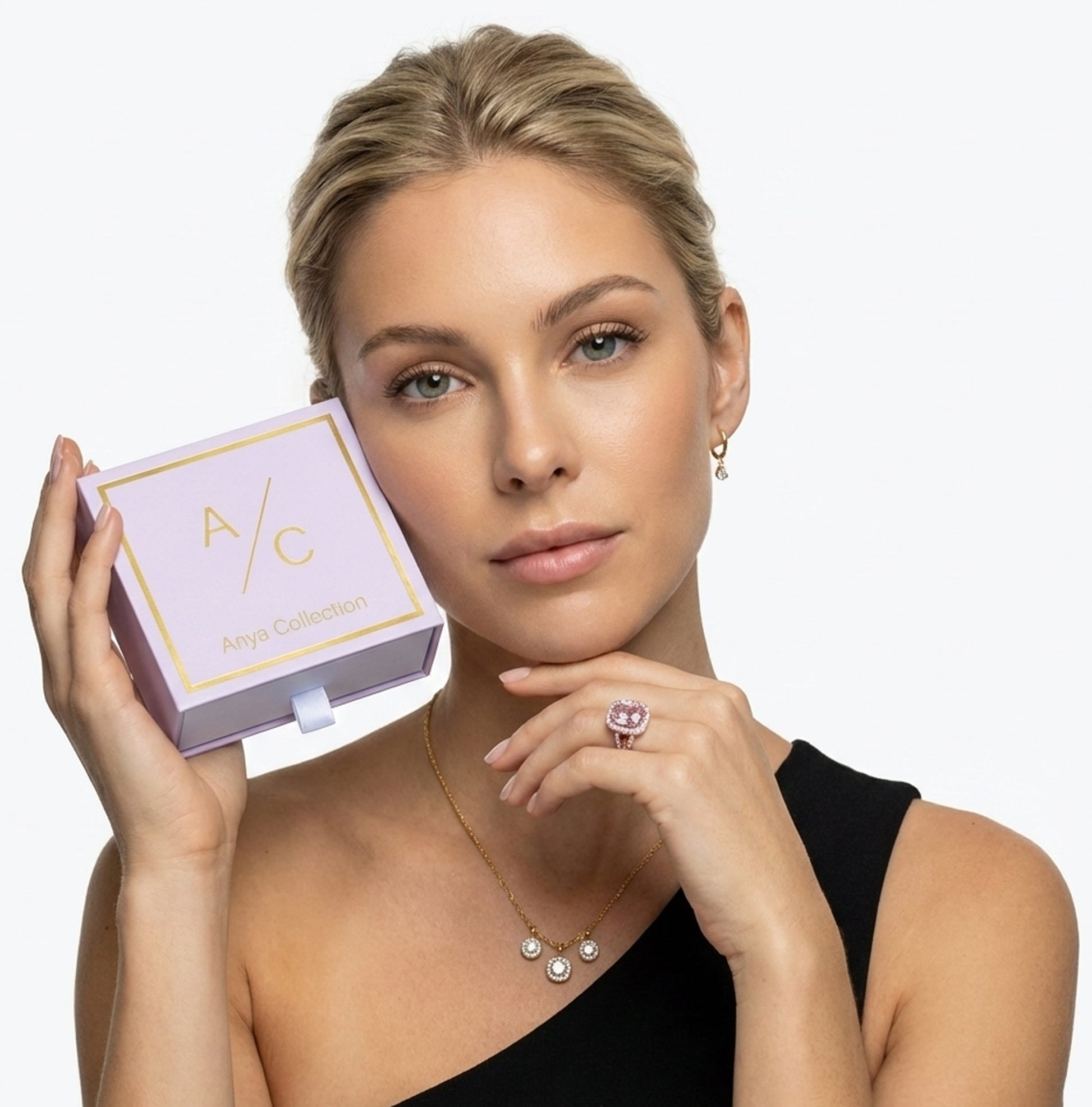 Woman holding a jewelry box with a necklace and ring, wearing a black dress against a white background