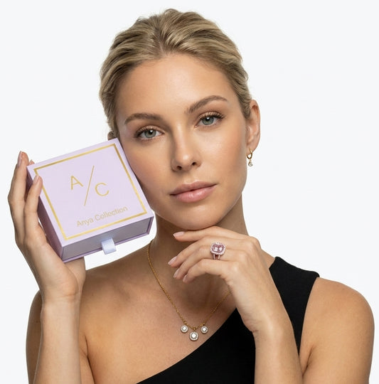 Woman holding a jewelry box with a necklace and ring, wearing a black dress against a white background