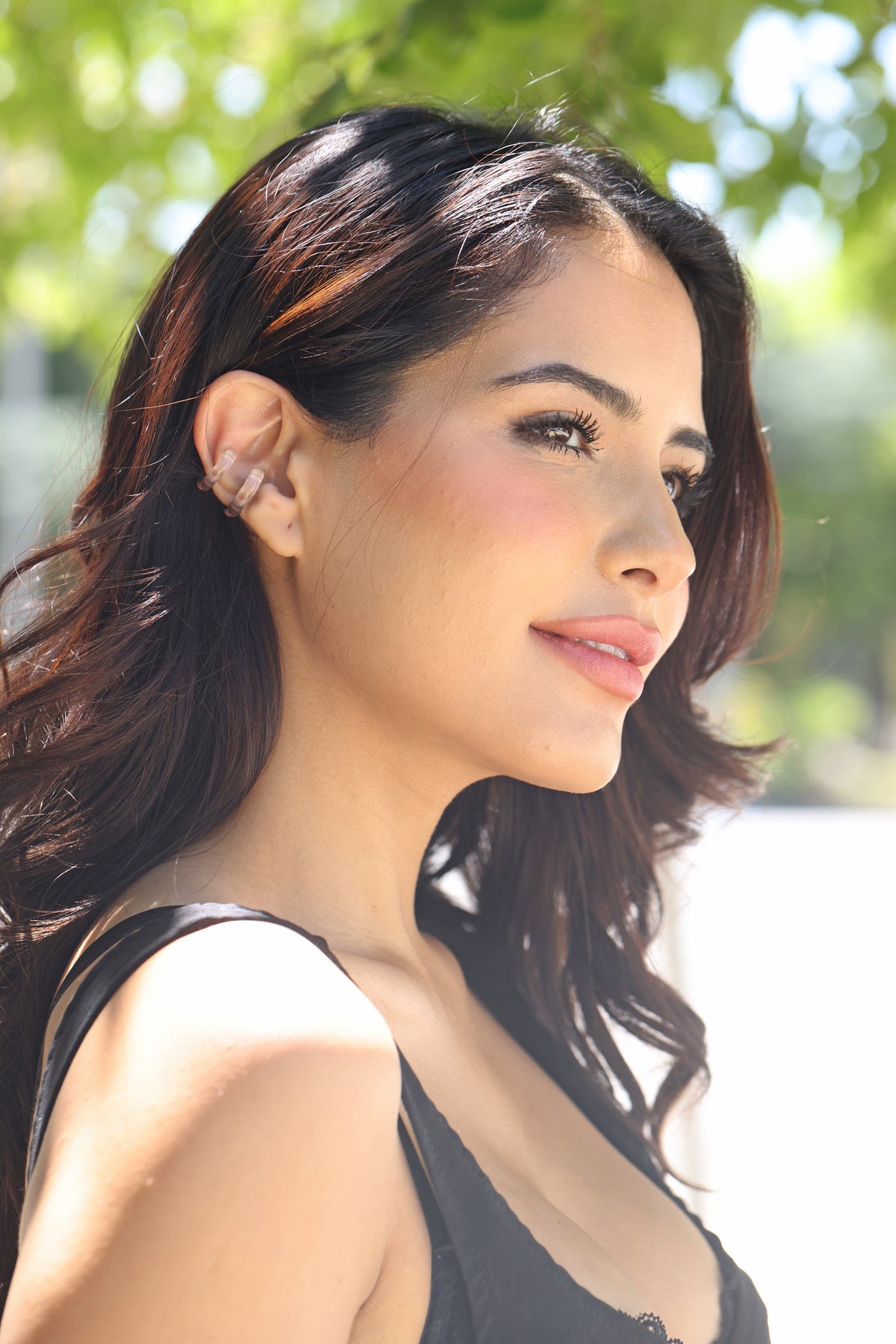 Woman with long dark hair  clear earrings and a black top outdoors