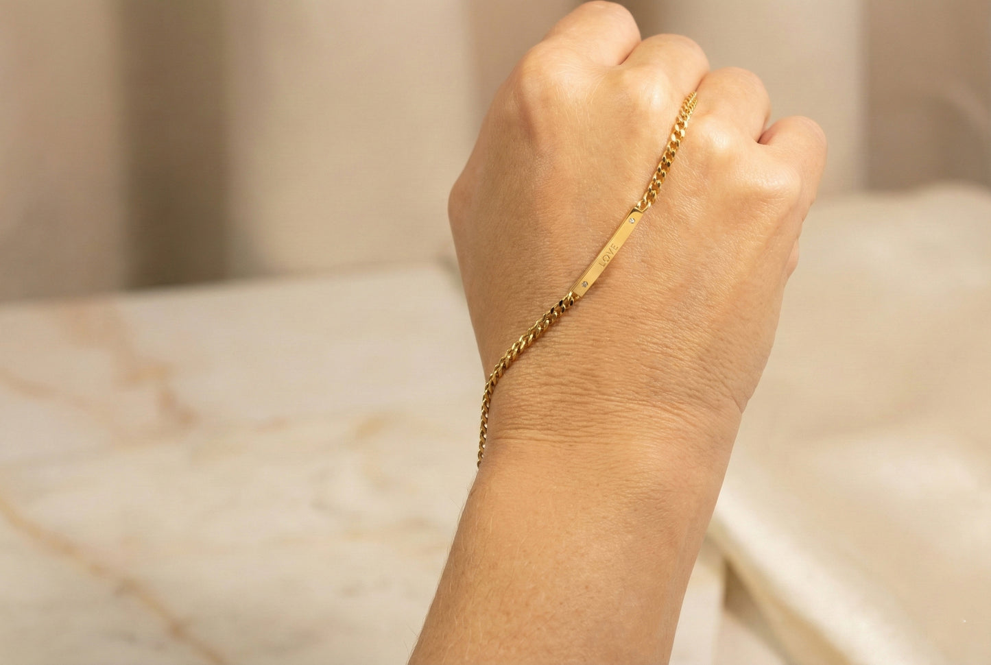 Hand wearing a gold bracelet on a marble surface