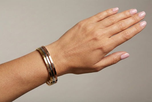Hand wearing an engraved gold bracelet on a neutral background