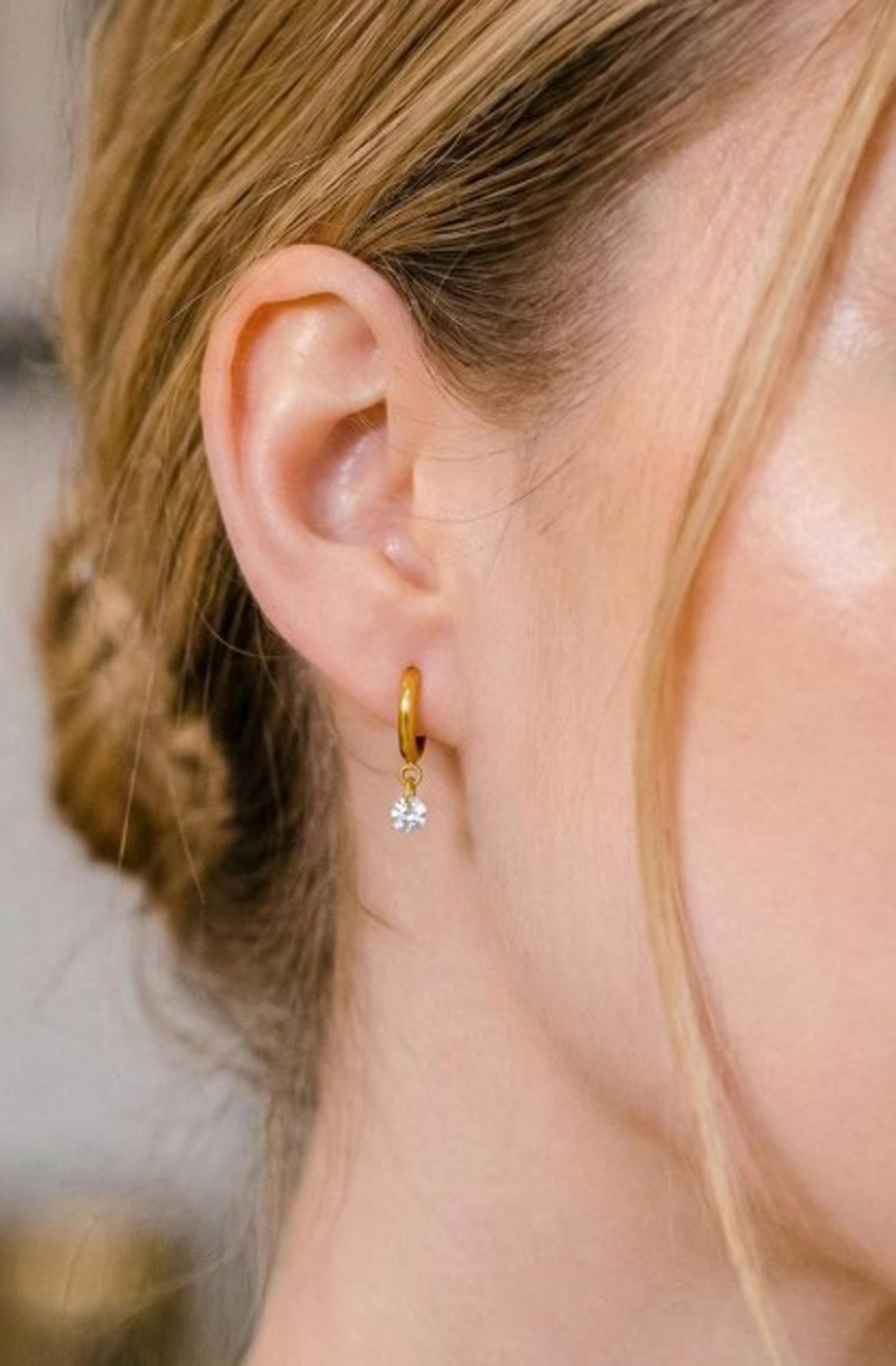 Close-up of a person wearing a gold hoop earring with a small diamond pendant.