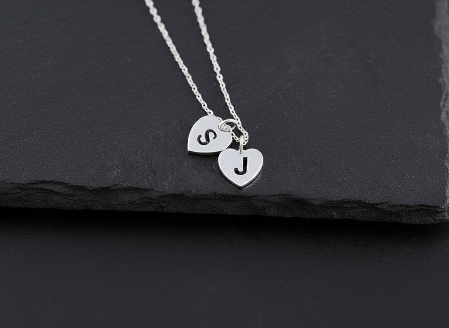 Silver necklace with heart-shaped pendants on a black slate background