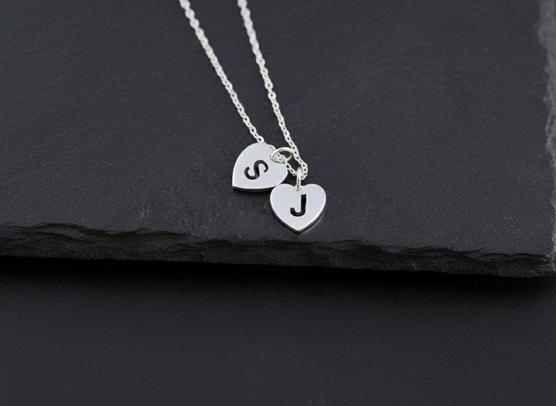 Silver necklace with heart-shaped pendants on a black slate background