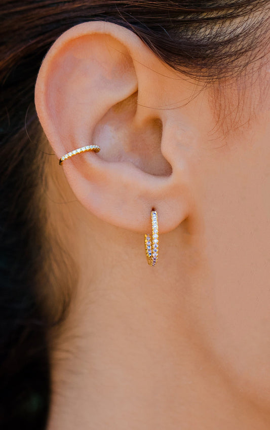 Close-up of an ear wearing gold hoop earrings with small stones.