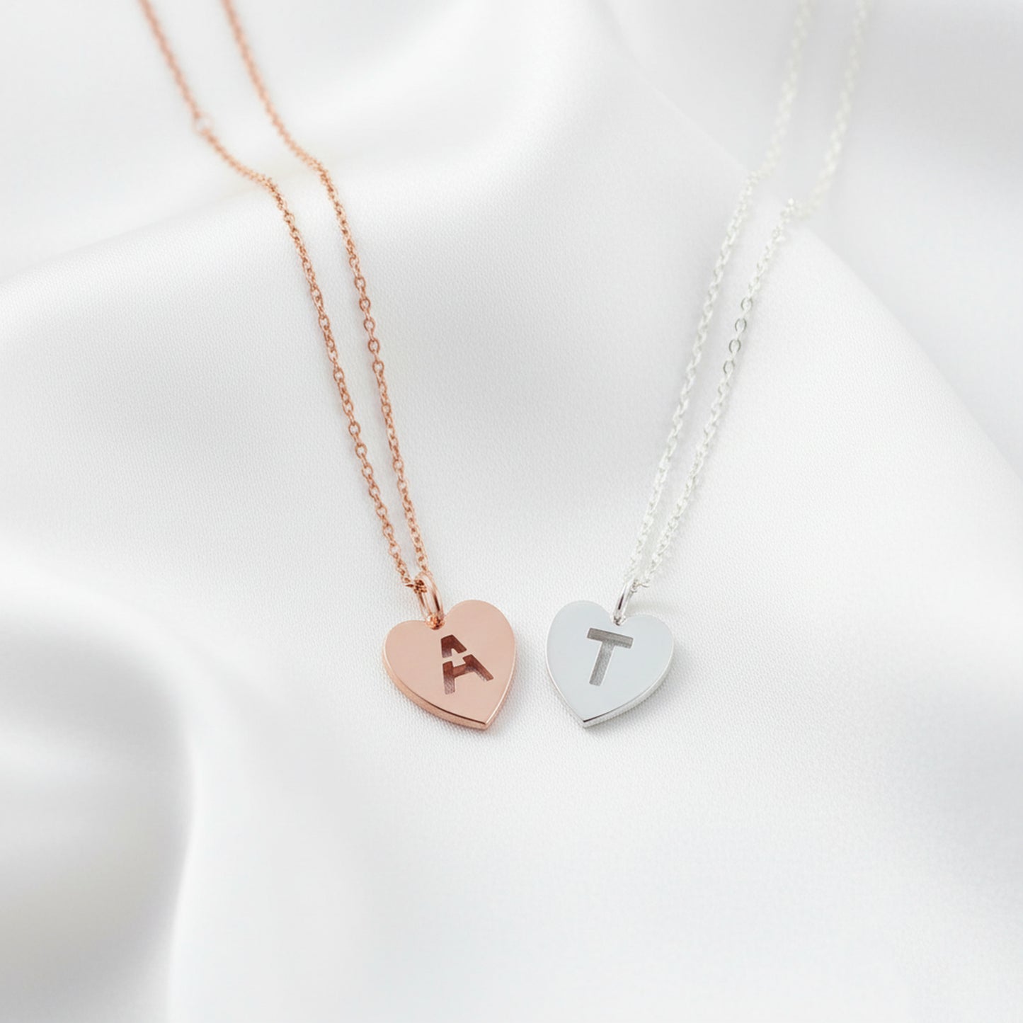 Two heart-shaped necklaces with initials on a white background