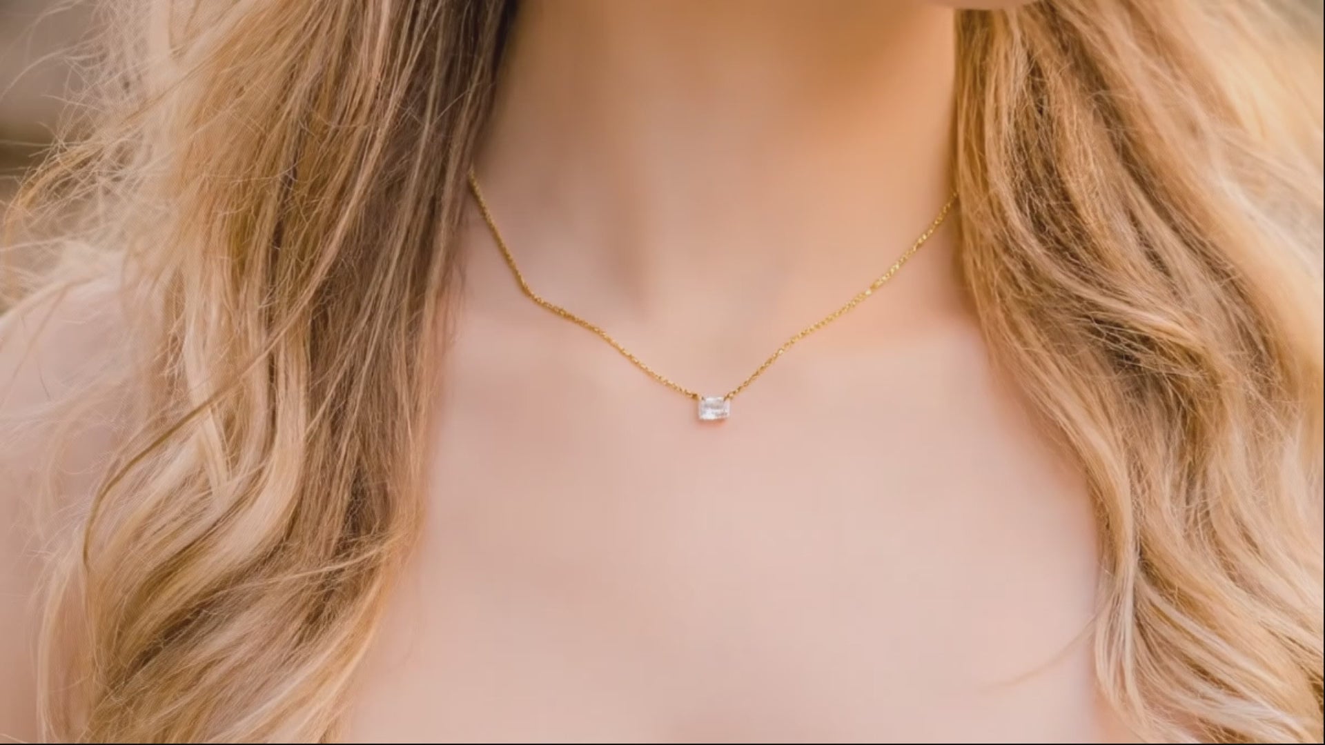 woman with long blond hair warring an emerald cut zircon with a gold chain