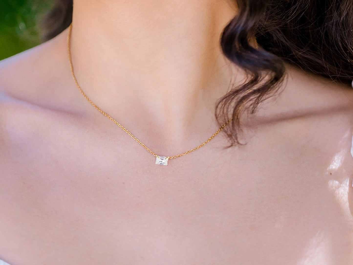 woman with long black hair warring an emerald cut zircon with a gold chain