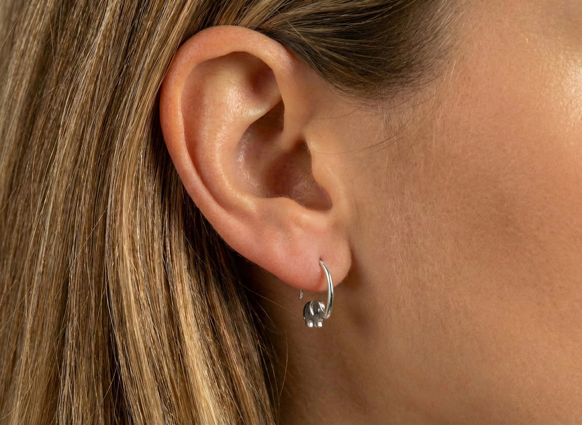 Close-up of an ear wearing a silver hoop earring with small round charms.