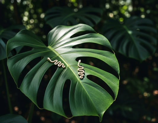Gold snake-shaped earring on a large green leaf with a blurred green background