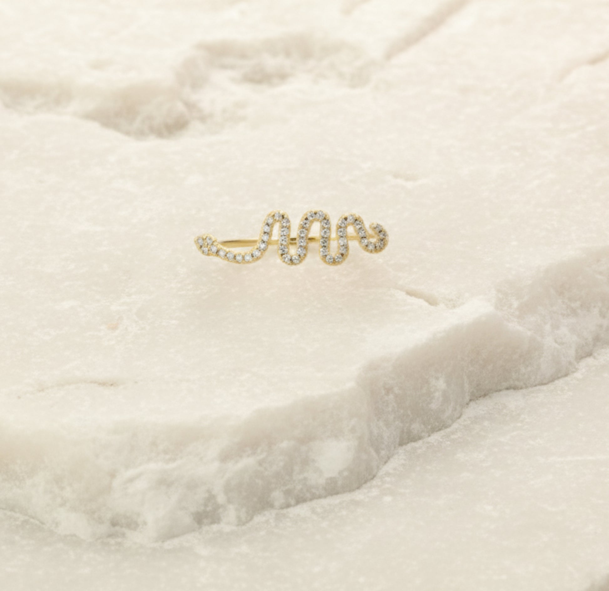 Snake earring with small diamonds on a soft beige fabric background