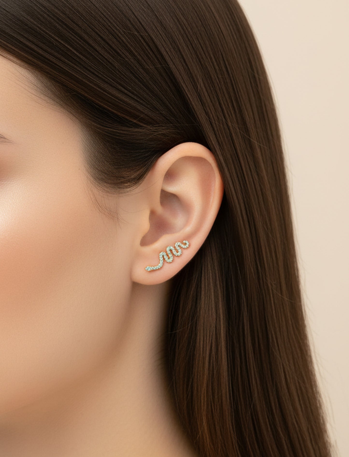 Close-up of an ear wearing a snake-shaped earring with a blurred background