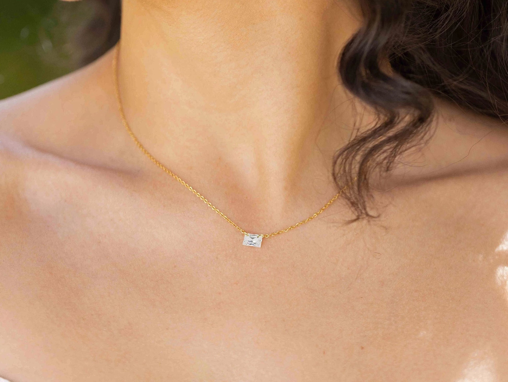 woman with long black hair warring an emerald cut zircon with a gold chain
