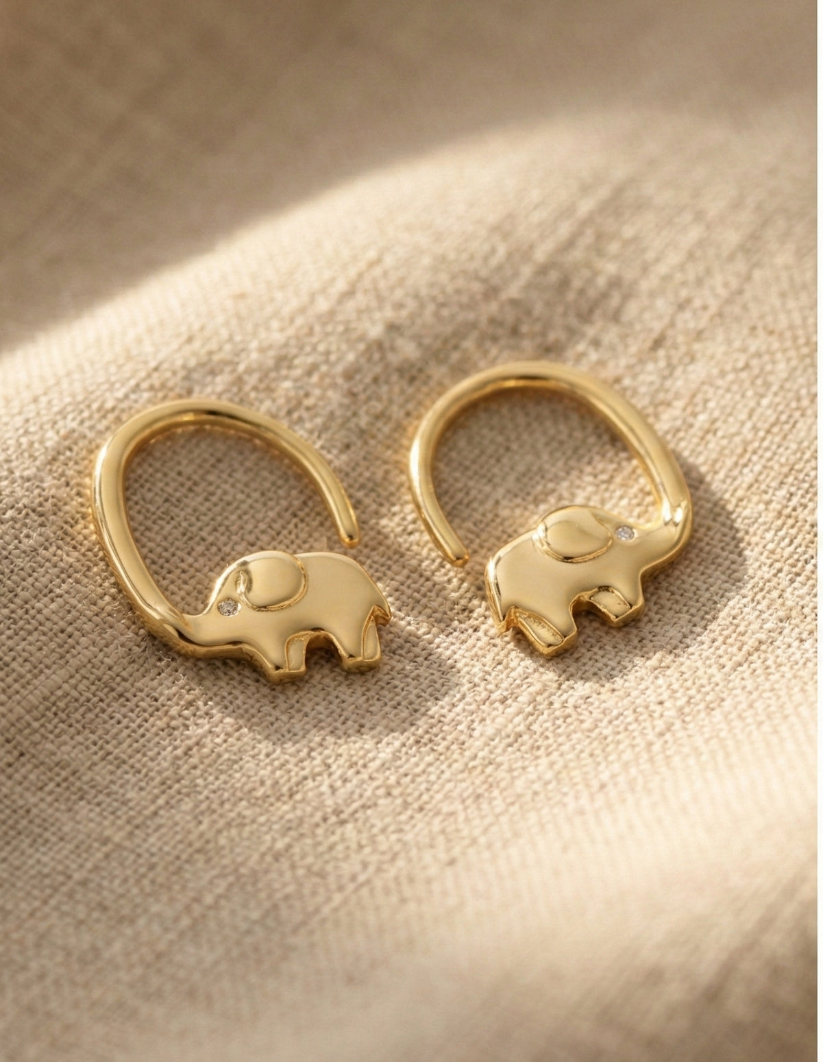 Gold elephant-shaped earrings on a textured beige surface