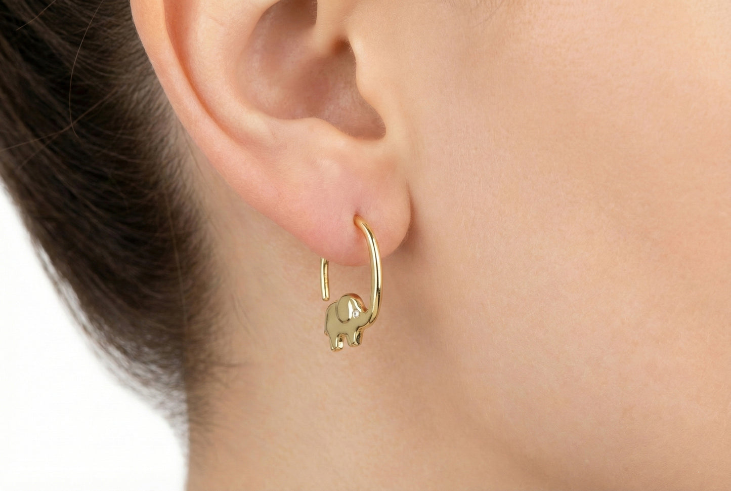 Gold hoop earring worn on an ear with a neutral background